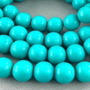 May include: A strand of turquoise beads, each bead is a bright, vibrant blue and round in shape.