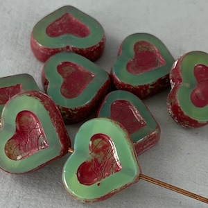 May include: A group of eight heart-shaped glass beads with a green outer layer and a red inner layer. The beads have a distressed, vintage look.
