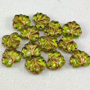 May include: A collection of green glass leaf beads with copper accents. The beads are shaped like maple leaves and have a glossy finish.