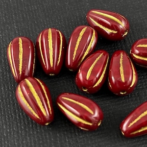 Könnte beinhalten: Eine Gruppe roter Glasperlen mit goldenen Streifen. Die Perlen sind tropfenförmig und haben eine glänzende Oberfläche.