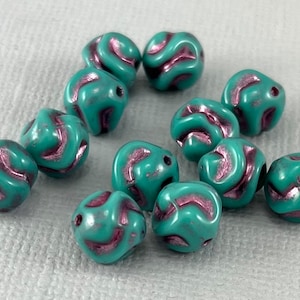 May include: A collection of 12 teal blue and pink swirl glass beads. The beads are round and have a textured surface.