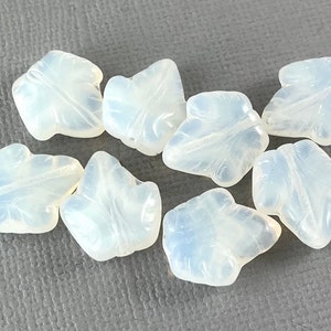 May include: Eight opaque white glass beads shaped like leaves. The beads have a smooth, polished finish.