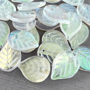May include: A pile of iridescent glass leaf-shaped beads with a silver-colored leaf design. The beads have a hole at the top for stringing.