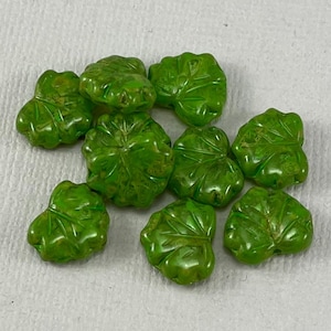 May include: A collection of green glass beads shaped like leaves. The beads have a textured surface and are perfect for jewelry making or crafting.