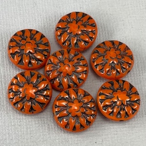May include: Seven orange and black round buttons with a floral design. The buttons are made of a smooth, hard material and have a glossy finish.
