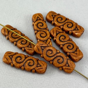 May include: Five brown ceramic beads with a swirl pattern. The beads are rectangular and have a textured surface.