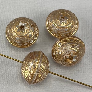 May include: Four decorative glass beads with gold and silver accents. Each bead has a star design on top and diamond patterns around the sides. A gold-colored wire runs through one of the beads.