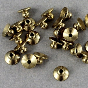 May include: A group of 18 gold-toned metal button covers with a round, raised knob on top. The button covers have a slightly flared, circular base.