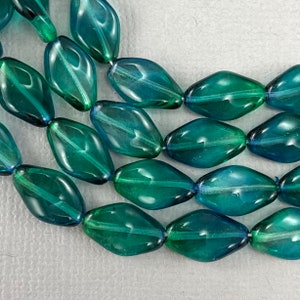 May include: A strand of teal and blue glass beads with a faceted oval shape. The beads are translucent and have a slight shimmer.