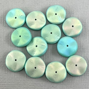 May include: Twelve iridescent teal green round buttons with a hole in the centre. The buttons have a textured surface and a slightly raised edge.