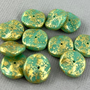 May include: A collection of 10 green and gold glass beads. The beads are flat and have a slightly irregular shape. They are decorated with gold flecks and have a hole in the centre for stringing.