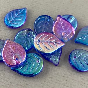 May include: A collection of iridescent glass leaf-shaped beads. The beads are primarily blue with hints of purple and gold, and feature a detailed leaf vein design. Each bead has a small hole for stringing.