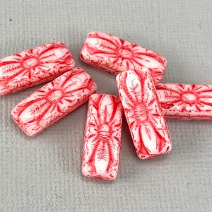Könnte beinhalten: Sechs rote und weiße Glasperlen mit einem floralen Muster. Die Perlen sind rechteckig und haben ein erhabenes Blumenmuster.