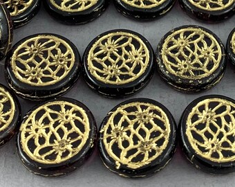 May include: A group of round, black glass beads with gold filigree designs. The beads have a shiny, glossy finish.