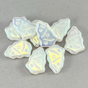 May include: A collection of iridescent, irregular-shaped beads. Each bead has a pearlescent finish with subtle color shifts. The beads have a tree-like design with small circular and linear details. The beads are scattered on a gray surface.