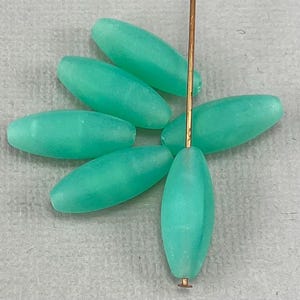 May include: A group of six oval-shaped, translucent, light green glass beads. The beads are arranged in a fan shape with a copper wire running through the center.