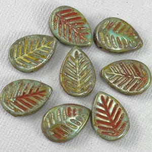 May include: A collection of eight leaf-shaped beads. The beads have a metallic green base color with red and yellow leaf vein details. The beads are teardrop-shaped and have a textured surface.