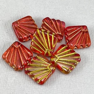 May include: Seven red and gold glass beads with a fan-shaped design. The beads are square and have a glossy finish.