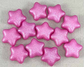 May include: A collection of eleven pink star-shaped sprinkles with a shimmering, glittery finish. The sprinkles are arranged closely together, showcasing their five-pointed design. These decorative sprinkles are ideal for adding a festive touch to baked goods.