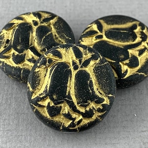 Könnte beinhalten: Drei runde schwarze Knöpfe mit einem erhabenen Design aus goldenen Blumen. Die Knöpfe haben einen Used-Look mit einer craquelé-Oberfläche.