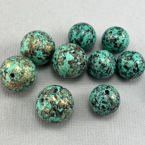 May include: Ten teal green and gold speckled round beads. The beads have a mottled, textured surface.