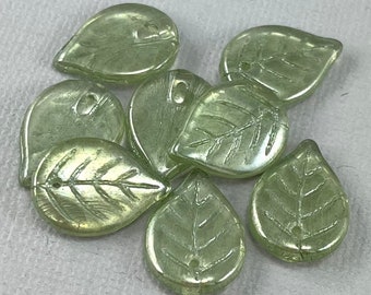 Op de afbeelding: Een groep van acht lichtgroene glazen kralen in de vorm van een blad met een reliëfpatroon van nerven. De kralen hebben een gat aan de bovenkant om aan te rijgen.