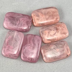 May include: Six pink and white swirled rectangular glass beads. The beads have a translucent appearance with a marbled effect.