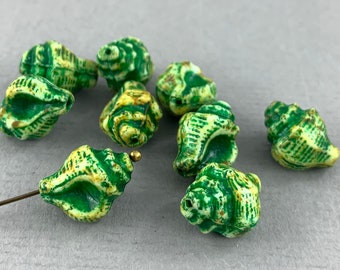May include: A collection of green and cream-colored seashell beads. The beads have a detailed, textured surface with a spiral design. The beads are on a gray surface.