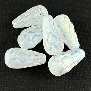 以下が含まれることがあります： 6つの虹色の涙型のガラスビーズ。各ビーズは、テクスチャ加工されたウェブのようなパターンと真珠のような光沢があり、さまざまな色を反射します。ビーズは暗い背景に配置されています。