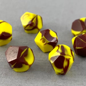 May include: Seven yellow and brown marbled faceted beads. The beads have a swirl pattern of yellow and brown.