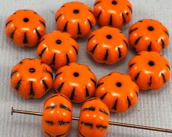 Puede incluir: Diez cuentas de vidrio naranja en forma de calabaza con detalles negros. Las cuentas están enhebradas en un alambre delgado.
