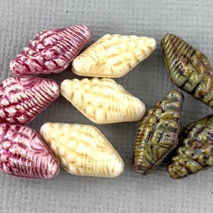Peut inclure: Un assortiment de perles décoratives en forme de petits coquillages. Les perles présentent une texture striée et sont disponibles en rose, crème et vert olive. Idéales pour la fabrication de bijoux et les projets d'artisanat.