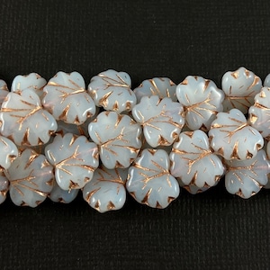 May include: A group of white glass leaf-shaped beads with gold accents. The beads are arranged in a random pattern.