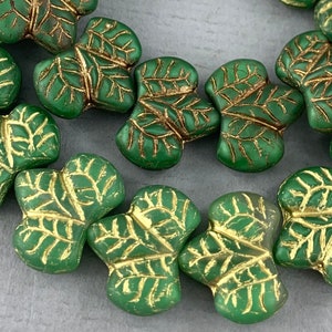 May include: Green glass beads with a gold leaf design. The beads are shaped like leaves and have a matte finish.