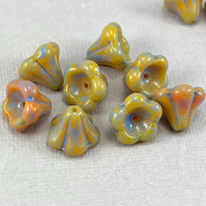 May include: A collection of flower-shaped beads in shades of yellow, orange, and blue. The beads have a glossy finish and a hole for stringing. These decorative beads are ideal for jewelry making and craft projects.