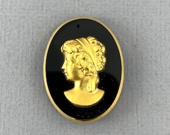 May include: A gold-colored cameo pendant with a profile of a woman with curly hair, set against a black background.