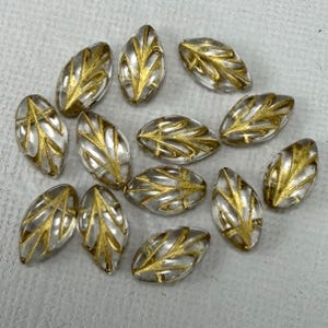 May include: Clear, leaf-shaped beads with gold leaf vein designs. These decorative beads are ideal for jewelry making and craft projects. The beads are oval-shaped and measure approximately 0.75 inches in length.