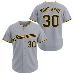 Könnte beinhalten: Ein hellgraues Baseball-Trikot mit schwarzen und goldenen Akzenten. Das Trikot zeigt den Text "Team name" und die Nummer "30" auf der Vorderseite sowie "YOUR NAME" und "30" auf der Rückseite. Es hat eine Knopfleiste und kurze Ärmel.