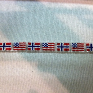 May include: A beaded bracelet with alternating American and Norwegian flags. The bracelet is white with red, white, and blue beads.