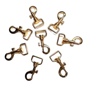 May include: Eight gold-toned metal swivel clasps with a spring-loaded gate. The clasps are commonly used for attaching straps, leashes, or other accessories.