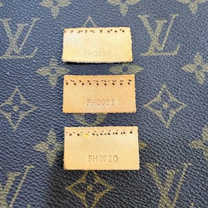 May include: Three small, rectangular tan leather tags with stitched edges and stamped text. The tags are arranged vertically against a brown background with a repeating pattern of interlocking letters. The text on the tags reads "FH0994", "FH0911", and "FH1920".