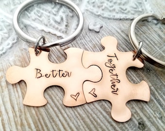 May include: Two copper-colored puzzle piece keychains. One piece reads "Better" and the other reads "Together". Each piece has a small heart etched on it. The keychains are attached to silver key rings.