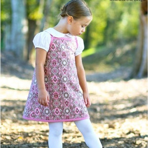 May include: A young girl wearing a pink and white patterned dress with a white collar, white tights, and black boots. The dress has a square neckline and a slightly flared skirt. The girl is standing in a wooded area with brown leaves on the ground. The text "Summertime Dreams" is written in black cursive at the top of the image. The text "mytreasuredheirlooms" is written in black cursive below the image. The text "Anastasia Cruz Designs" is written in black cursive below the text "mytreasuredheirlooms".