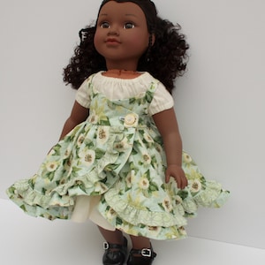 May include: A dark-skinned doll wearing a green and white floral dress with a white underskirt and black shoes.