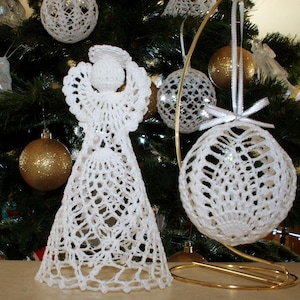 May include: A white crocheted angel figurine with a halo and a wide, flared skirt, positioned next to a white crocheted spherical ornament hanging from a gold-colored metal stand. Both items feature intricate, open-work lace patterns.