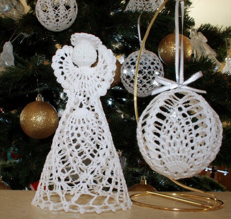 May include: A white crocheted angel figurine with a halo and a wide, flared skirt, positioned next to a white crocheted spherical ornament hanging from a gold-colored metal stand. Both items feature intricate, open-work lace patterns.