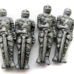 May include: Four silver-colored miniature knight figurines, each holding a sword and wearing armor. The knights are standing in a row on a white surface.