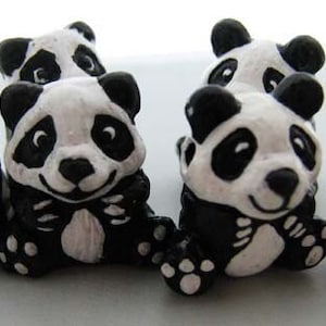 May include: A set of six small black and white panda figurines. The pandas are sitting with their paws in front of them and have a smiling expression.