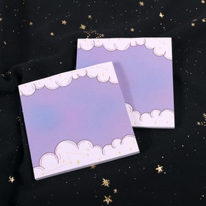 May include: Two purple and white sticky note pads with a cloud and star design. The pads are on a black background with gold glitter stars.