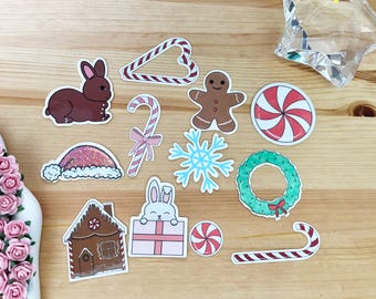 May include: A set of 11 Christmas-themed stickers featuring a gingerbread house, a candy cane, a snowflake, a wreath, a peppermint candy, a gingerbread man, a bunny holding a gift, a Santa hat, a brown rabbit, and two candy canes.